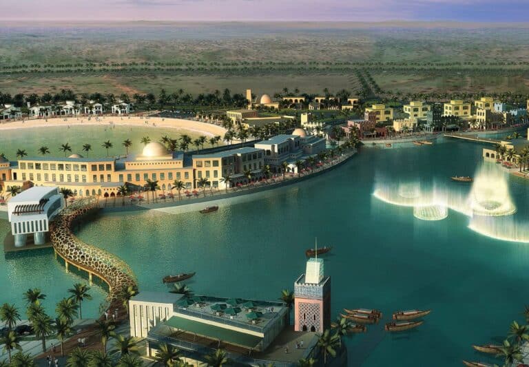 Traditional-style buildings and modern arched bridge over a man-made lagoon with illuminated water features at Dana Bay, Saudi Arabia.