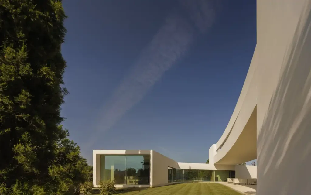 A house that melts into the garden: a modern architectural design in Madrid blending curved white walls and green spaces through open voids and wide glass facades.