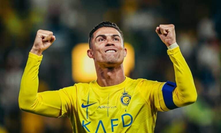 Cristiano Ronaldo in Al Nassr FC yellow jersey celebrating with raised fists during a match under stadium lights.