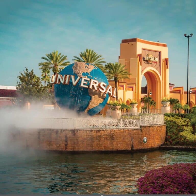 The iconic globe sculpture at the entrance of Universal Orlando Resort, surrounded by palm trees and mist under a clear sky.