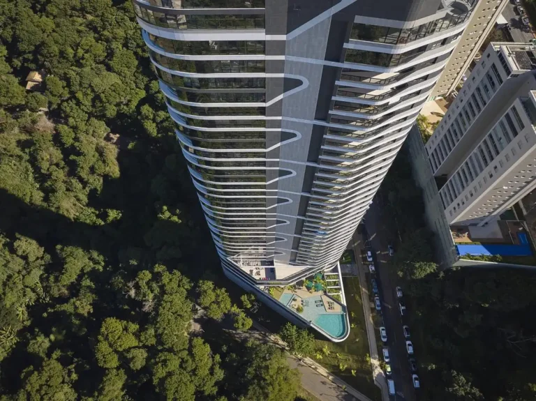 Aerial view of Edifício Miró Tower in Buenópolis, Minas Gerais, showcasing its curved glass facade and integration with surrounding forested terrain.