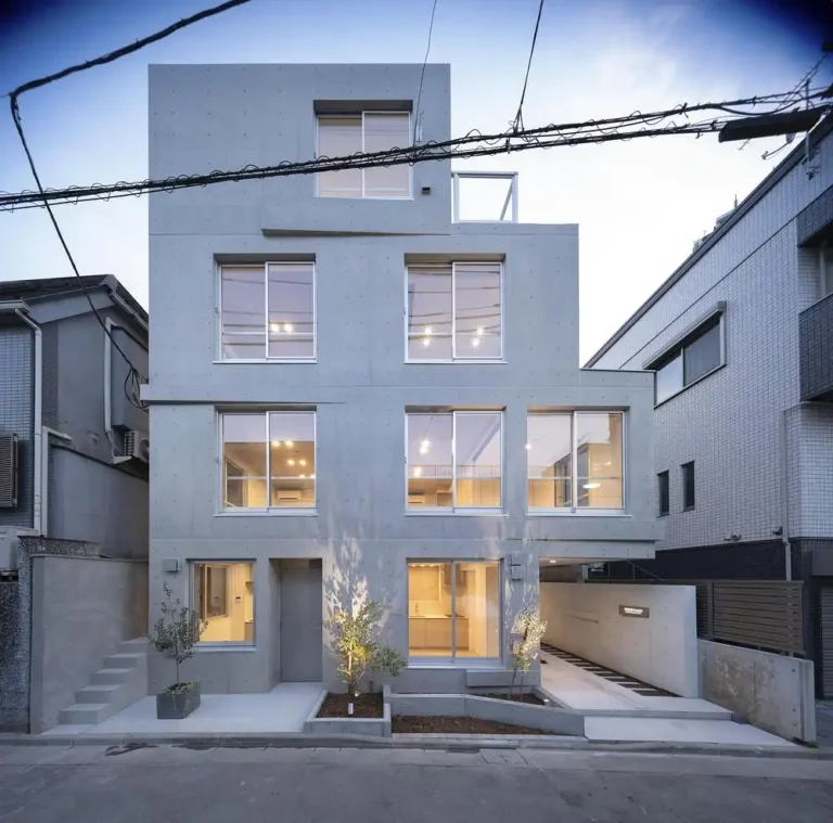 Exposed concrete facade of a multi-unit residential building in Tokyo’s Meguro ward, featuring staggered windows and minimal landscaping.