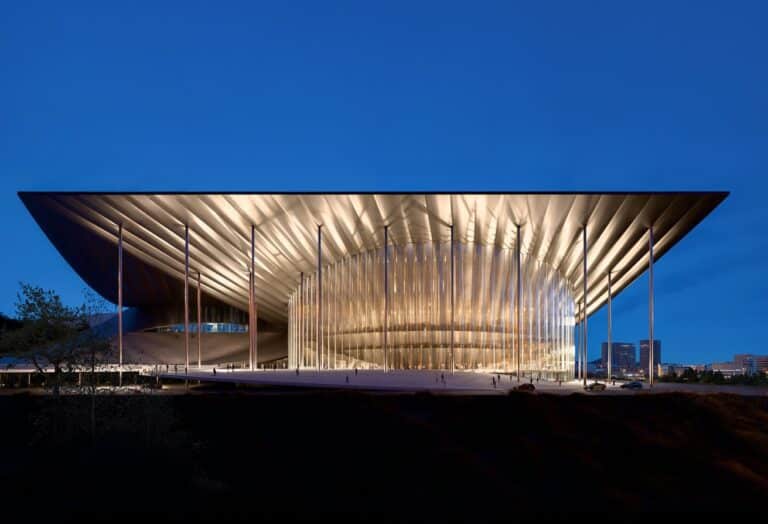 Ulsan Performing Arts Venue at dusk, featuring a cantilevered roof and vertical light elements framing the entrance. The architectural design integrates public space with performance infrastructure.