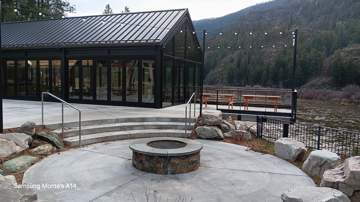 River Edge Pavilion exterior with glass walls, fire pit, and riverfront view in Montana’s forested canyon.