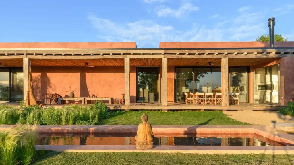 Earthy walls blend with twilight glow, wooden gallery opens to landscape and pool.