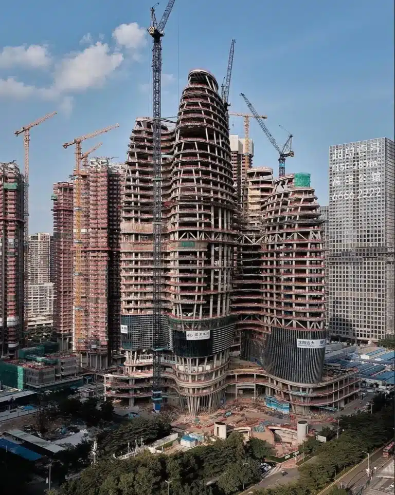 Aerial view of a multi-tower structure under construction in Shenzhen, surrounded by cranes and urban development.