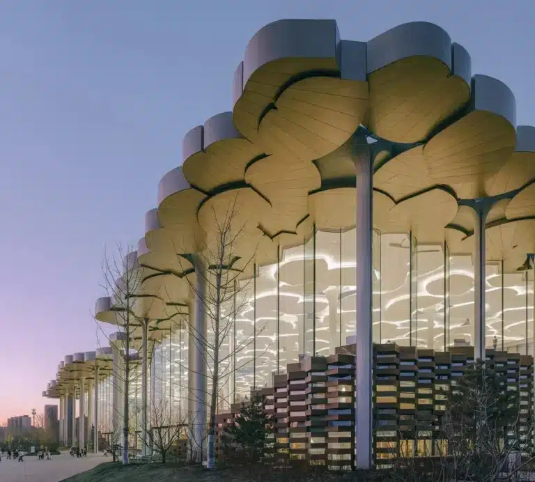 Beijing Library exterior at dusk, featuring its distinctive layered canopy and glass facade with internal lighting visible.