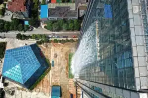 Aerial view of the Liebian International Building in Guiyang, China, showing its glass facade and a 108-meter artificial waterfall cascading down one side during activation. The surrounding urban context includes adjacent structures and a street with parked cars.