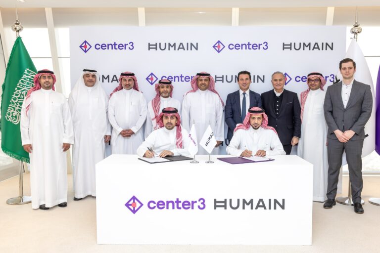Signing ceremony for the AI data center project between Humain and Center3, with executives in traditional Saudi attire and business suits against a branded backdrop.