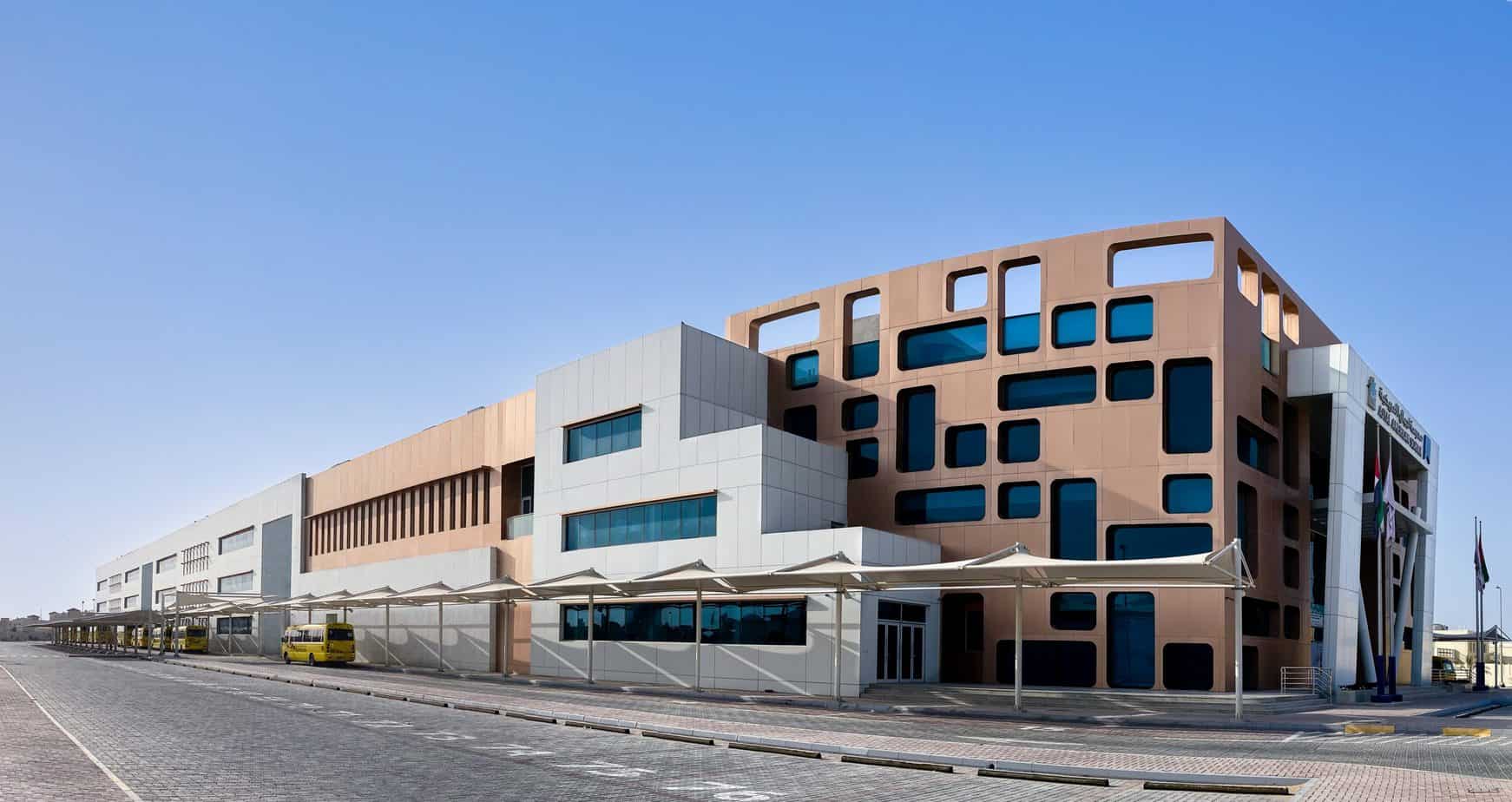 Modern multi-story school building in the UAE with a distinctive terracotta facade featuring irregular rectangular windows and white architectural accents.