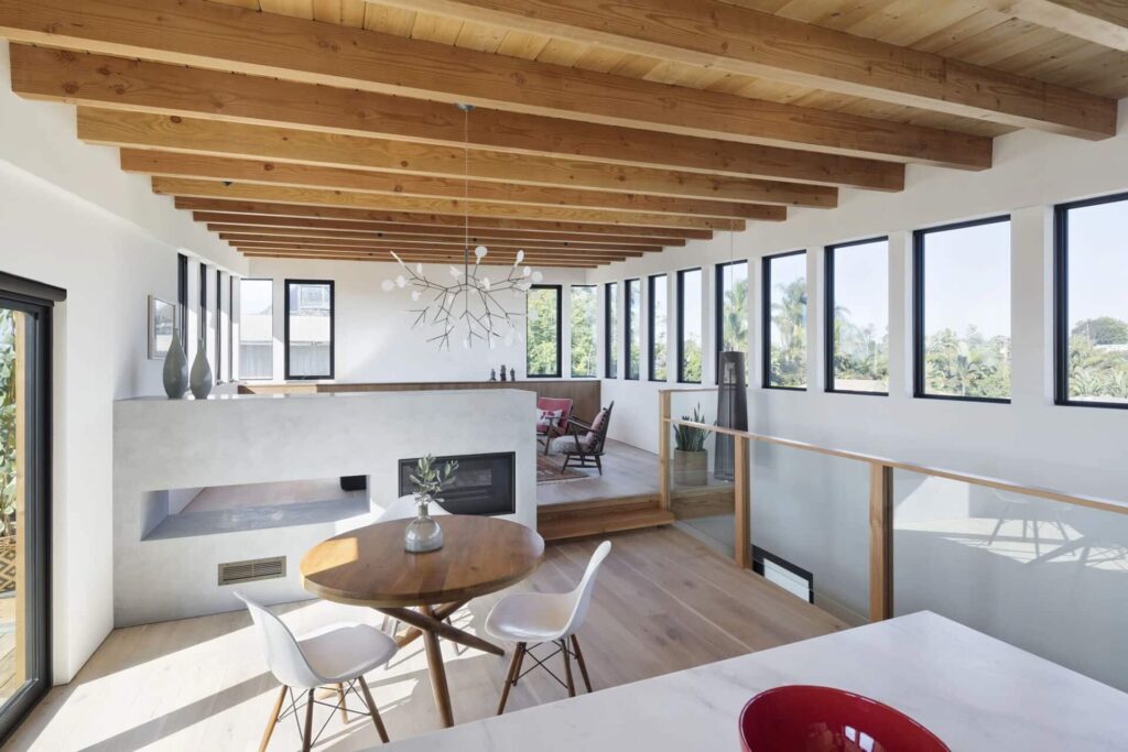تصميم داخلي مودرن لغرفة طعام ومعيشة مفتوحة مع سقف بآرواق خشبية ظاهرة ونوافذ كبيرة توفر إضاءة طبيعية وافرة.
