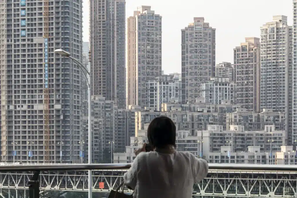 منظر خلفي لشخص يتكئ على حاجز ويطل على أفق مدينة كثيفة يضم العديد من المباني السكنية شاهقة الارتفاع.