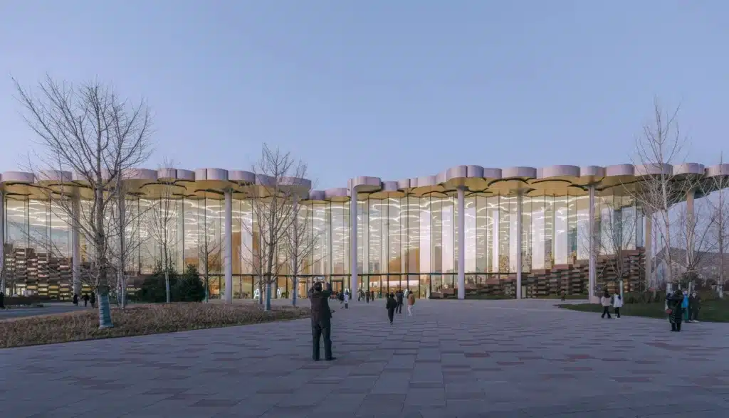 Beijing Library facade at twilight, showing its glass curtain wall and sculptural canopy with visitors on the plaza.