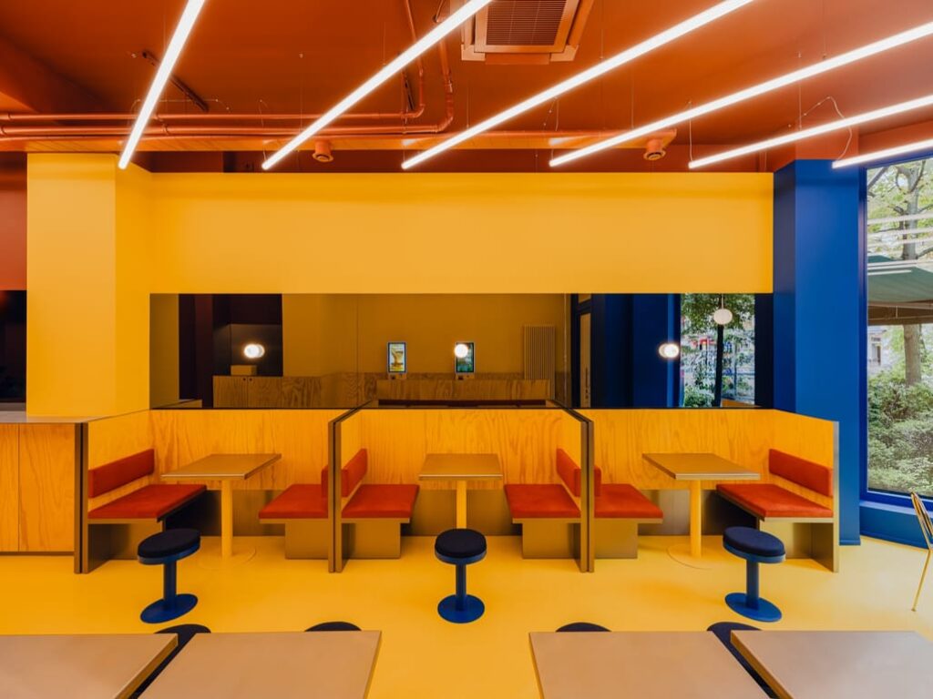 Linear lights glow over yellow walls and warm red seating, guiding the visitor&rsquo;s path.