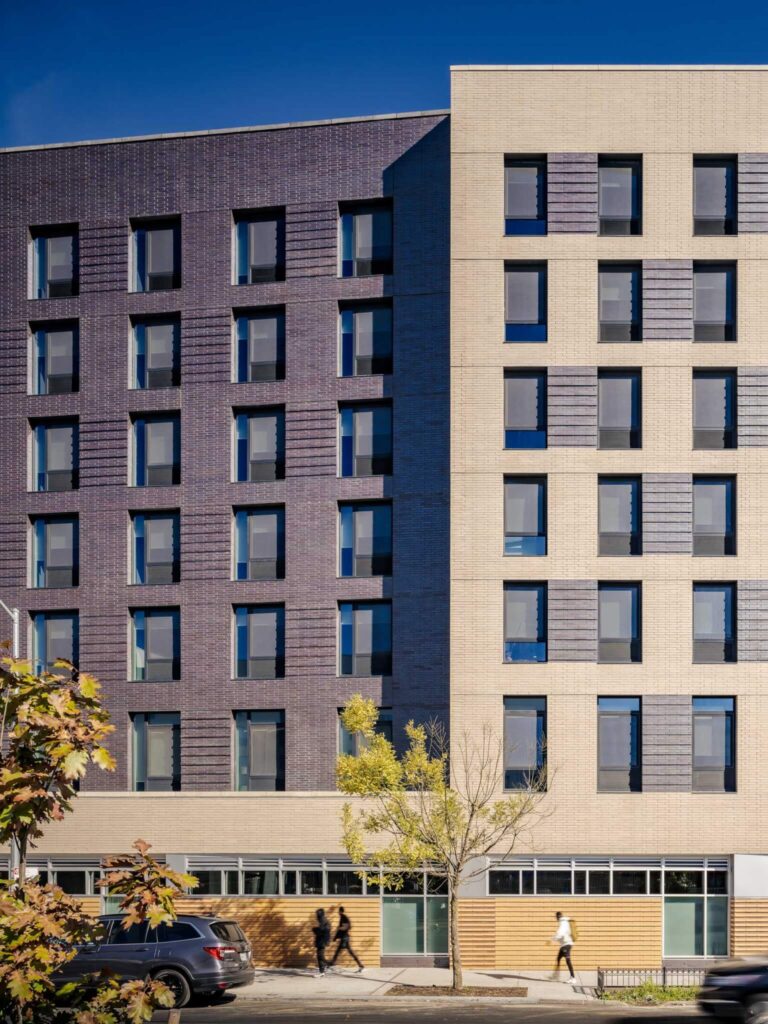 Close up shot of the contrasting brick residential facades (charcoal and beige), showing punched windows and the orange brick industrial podium base, central to the Vertical Integration of Industry and Housing design.