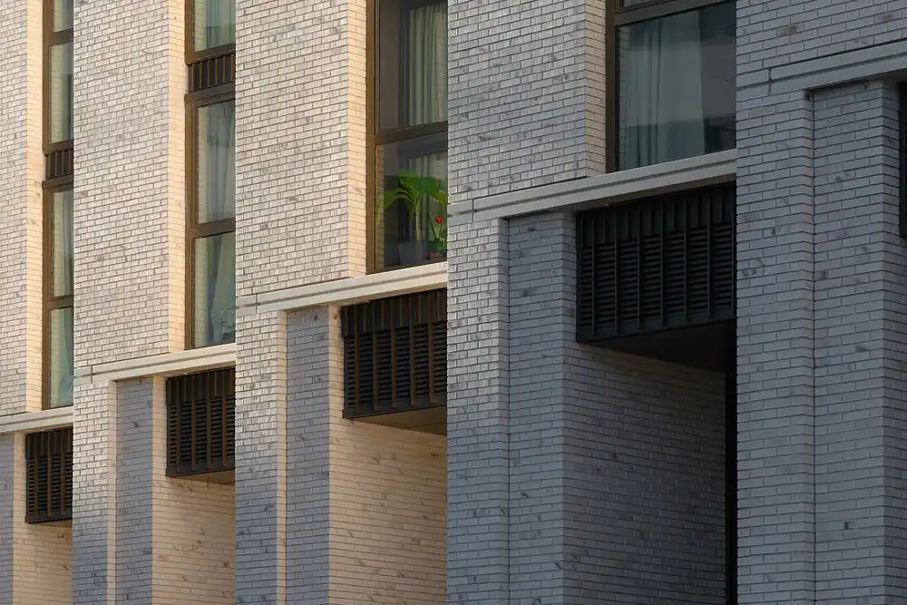 Sharp brick serrations create a dramatic light and shadow contrast, adding tectonic depth to the facade.