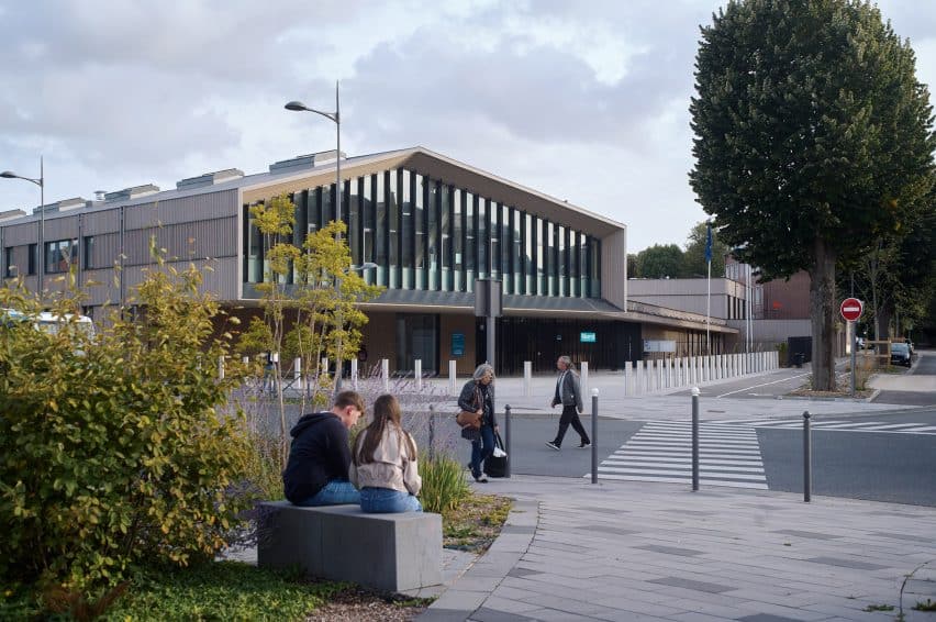 Exterior facade of the timber-framed school in Cambrai, showing its contemporary design with vertical glass bands and front green spaces where students sit.