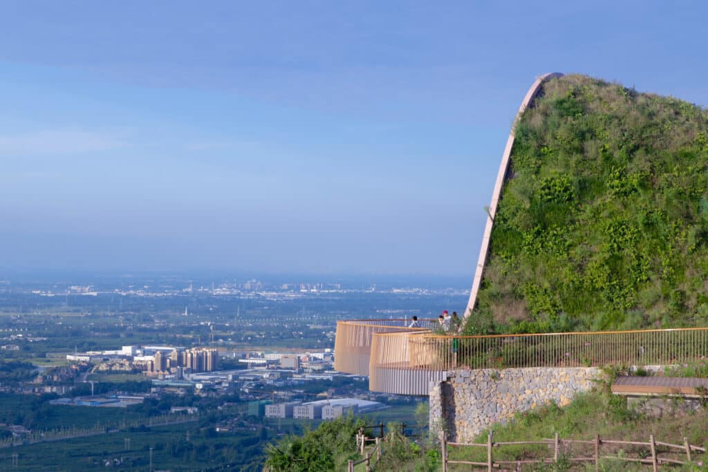 Pujiang Platform in Chengdu, a timber pavilion covered with earth overlooking the city and plains, featuring an open walkway and stone retaining wall.