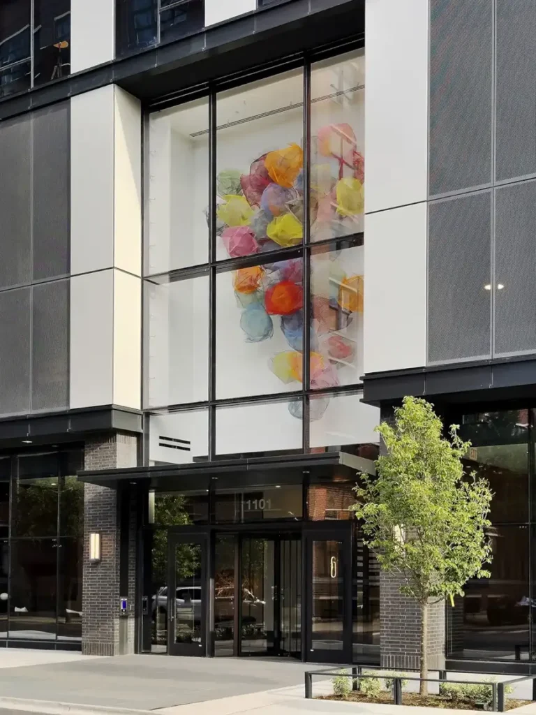 Entrance of Coppia Tower in Chicago's West Loop, featuring a vibrant contemporary art installation displayed within the glass façade above the main lobby doors.