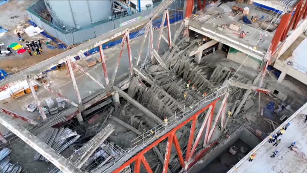 مشهد جوي لانهيار مكتبة غوانغجو، يظهر فيه الهياكل الفولاذية الحمراء المائلة والخرسانة المتكسرة بين طوابق البناء، مع فرق الإطفاء التي تتفقد موقع الحادث الذي أودى بحياة أربعة عمال.