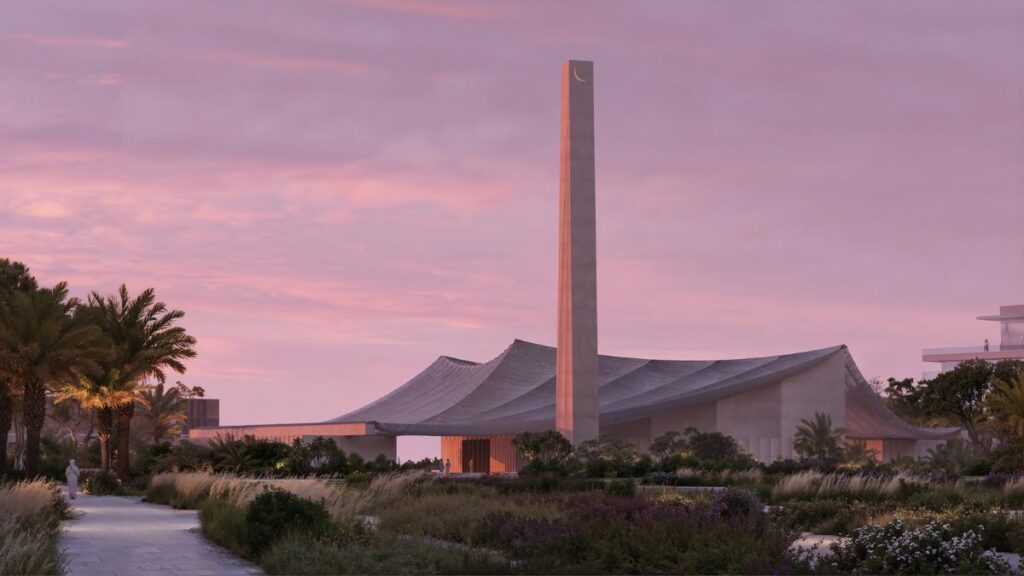 Palm Jebel Ali Friday Mosque at sunset, showcasing its 40-meter minaret with crescent finial and sweeping canopy against a pink sky, surrounded by native landscaping and palm trees.