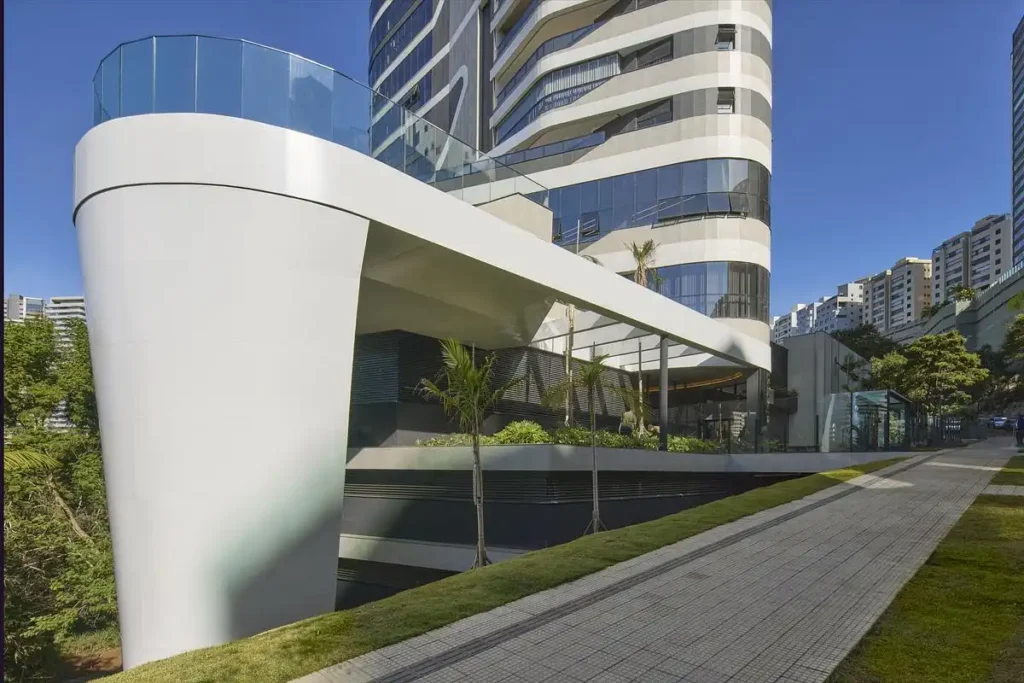Entrance to Edif&iacute;cio Mir&oacute; Tower featuring sculptural canopy above duplex typology units, with landscaped walkway and palm trees.