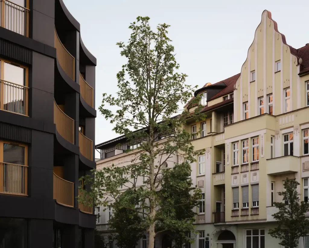 Close up of a contemporary black building with curved balconies adjacent to a historic cream colored tenement.