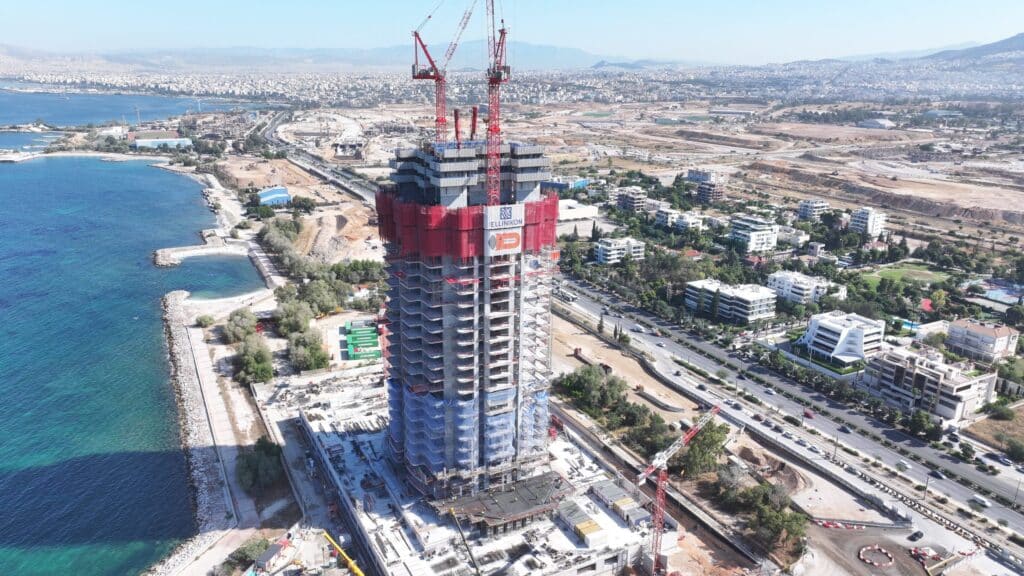 Residential tower under construction showing its concrete structure against the backdrop of the sea and mountains.