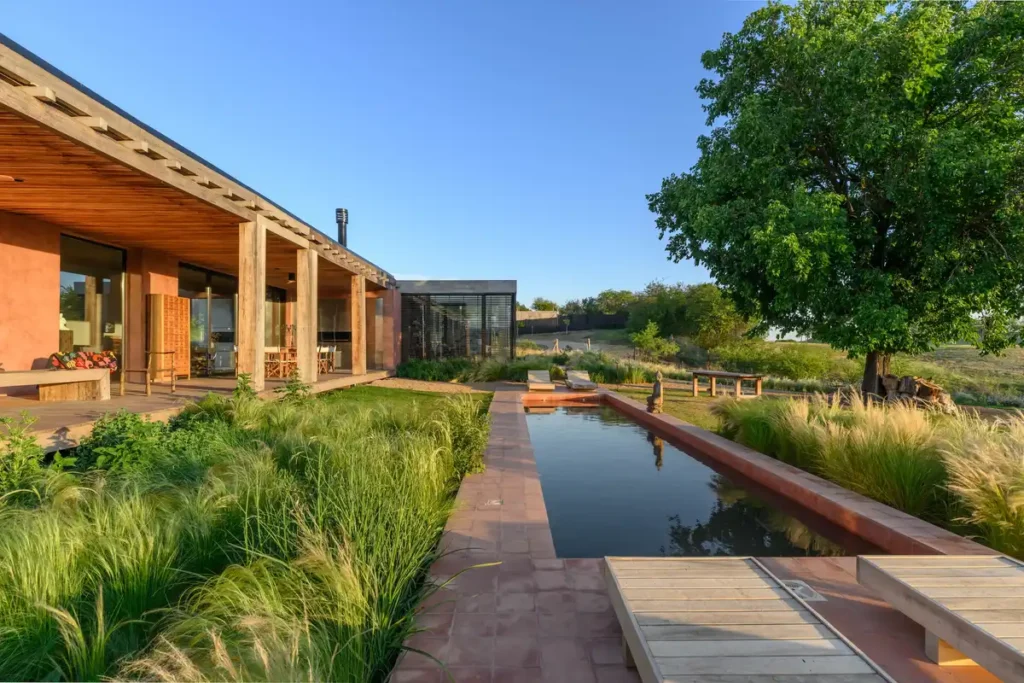 Stone path winds through grasses to pool, tree shadow caresses earth-toned walls.