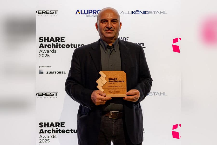 Palyan Architects&rsquo; representative holds the SHARE Architecture Awards 2025 Honorable Mention trophy at the ceremony, with event branding visible in the background.