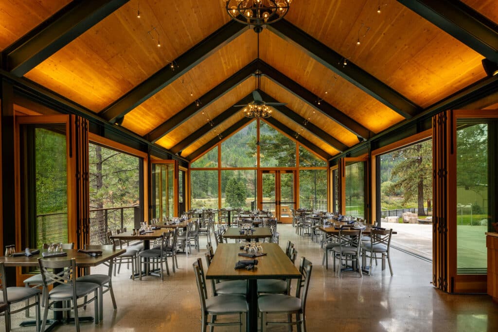 River Edge Pavilion interior with vaulted wood ceiling, steel trusses, and floor-to-ceiling windows framing forest views.
