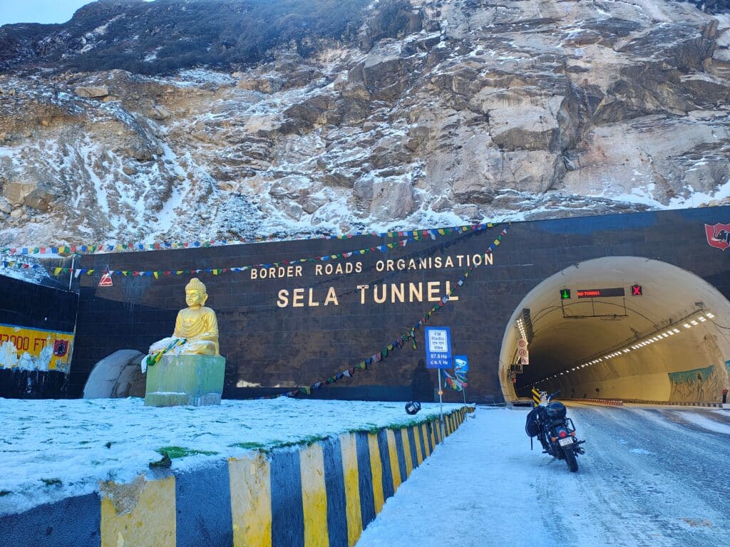Sela Tunnel entrance in winter, showcasing India&rsquo;s Border Infrastructure with a golden Buddha statue, prayer flags, and snow covered Himalayan terrain.