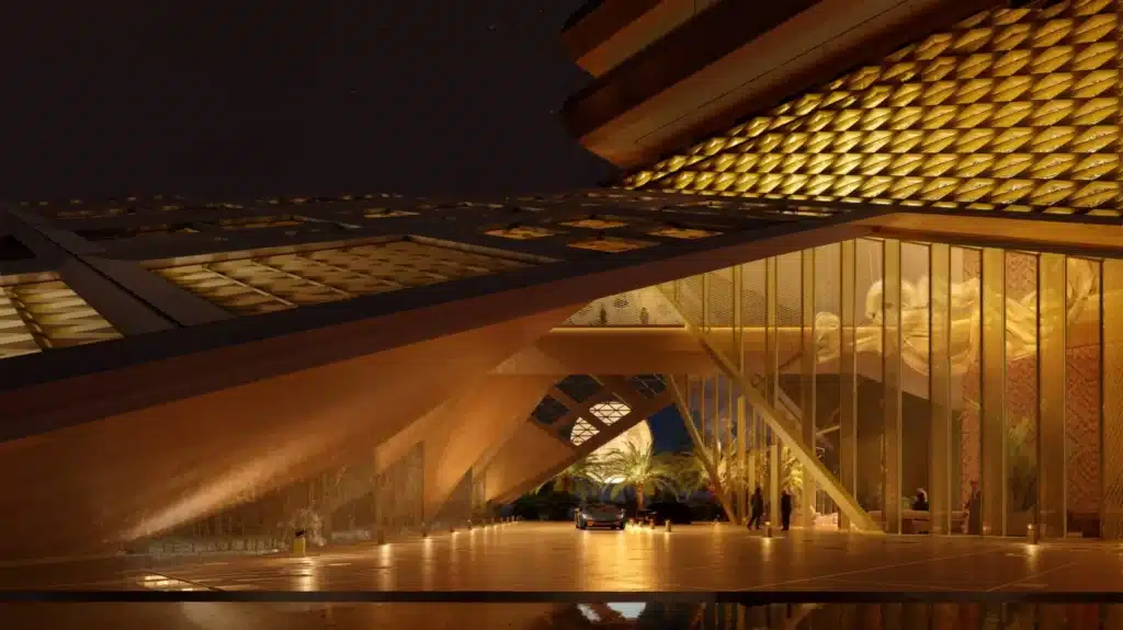 A nighttime view of a luxury hotel entrance under a geometric canopy, with warm lighting illuminating the facade and reflecting on the wet pavement.