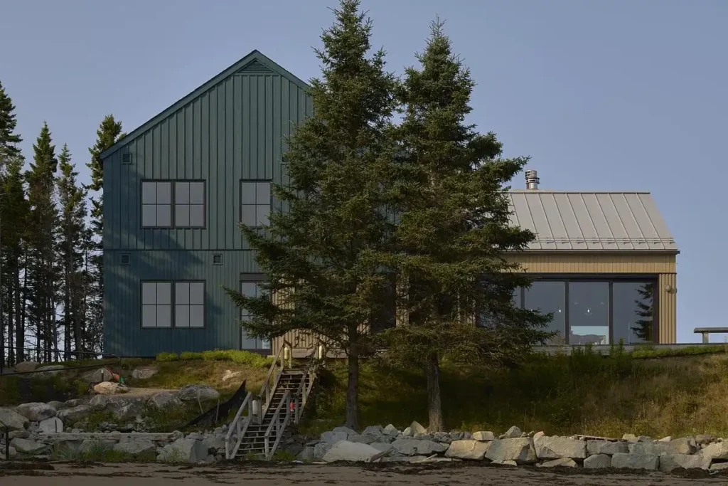 مبنى أخضر داكن يرتفع بين الصخور والأشجار، يعكس تدرجات السماء الهادئة.