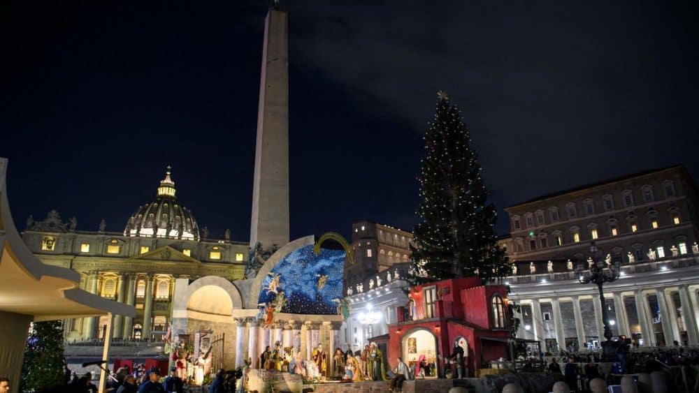 Architecture and temporary installations merge in St. Peter&rsquo;s Square: Nativity scene and Christmas tree framed by historic obelisk and Basilica at night.