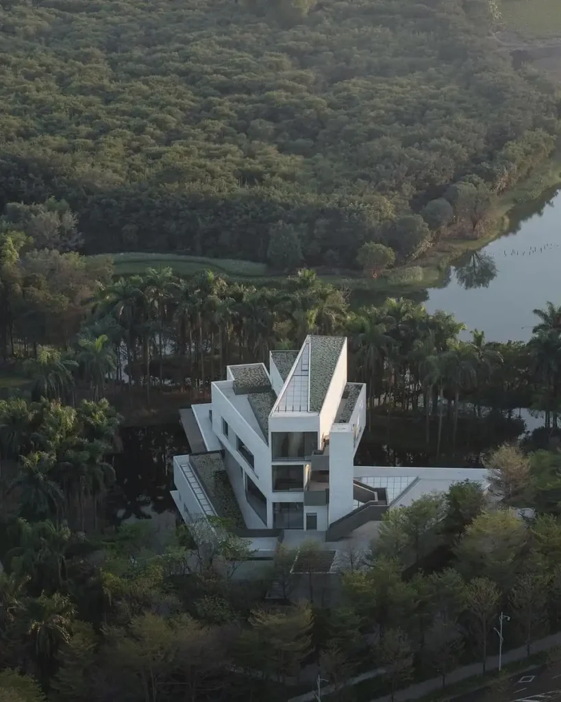 Aerial shot showing white concrete volumes rotating around a central atrium, surrounded by forest and open wetlands.