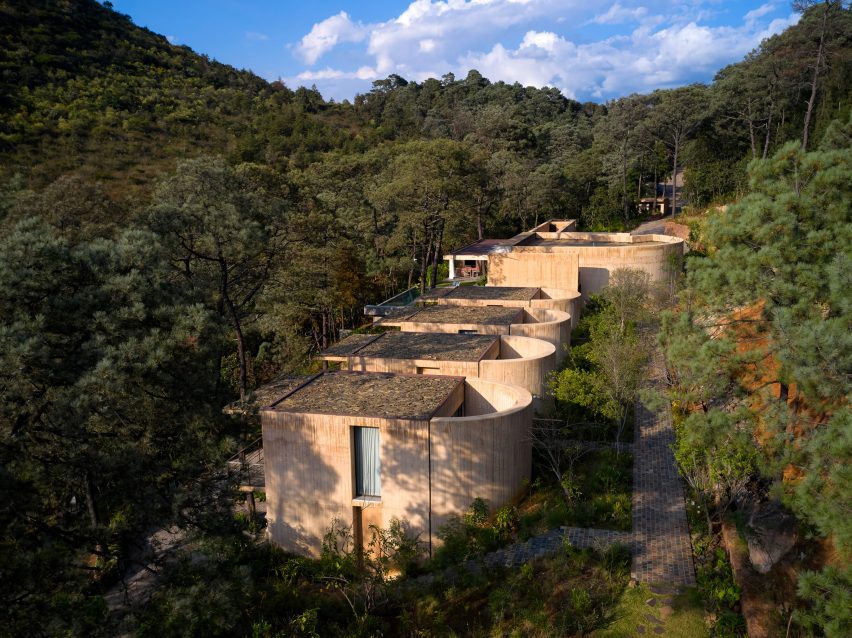 Slanted aerial shot emphasizing the rear curves of the Segmented Concrete Pavilions and their strong integration with the Valle de Bravo forest.