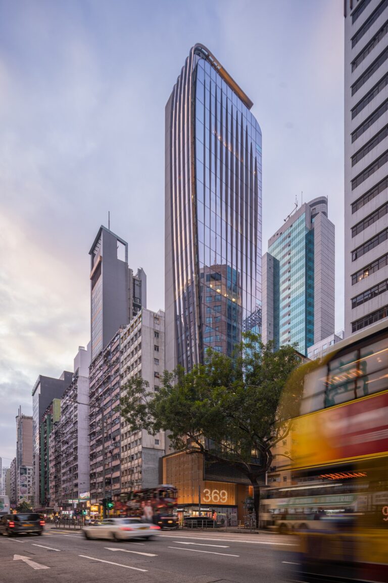 Modern office tower in Hong Kong with a curved glass facade reflecting surrounding buildings, set against the active traffic of Hennessy Road.