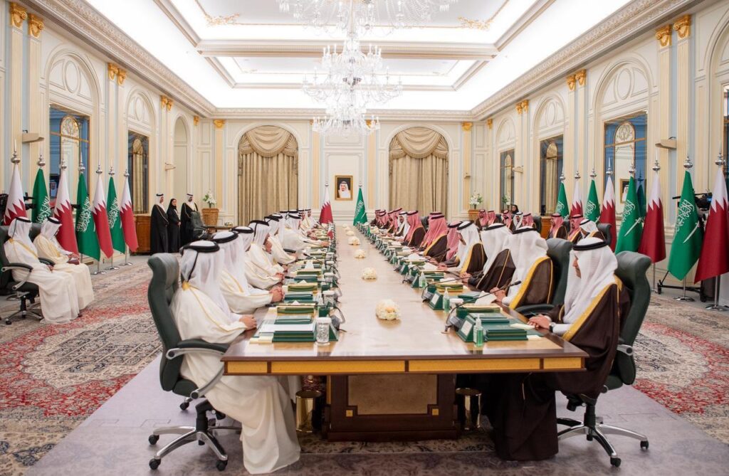 Image documenting Saudi and Qatari official delegations during consultation sessions to activate the High Speed Electric Rail Link agreement, held in a grand governmental meeting hall.
