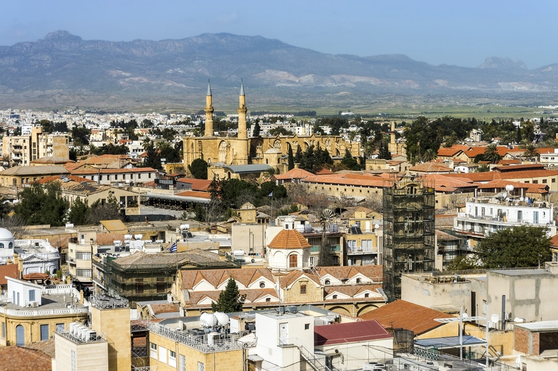 Aerial view of Nicosia, Cyprus, showcasing the Selimiye Mosque amidst residential neighborhoods and historic buildings, with mountainous backdrop, within the context of the carbon-neutral diplomatic headquarters project.