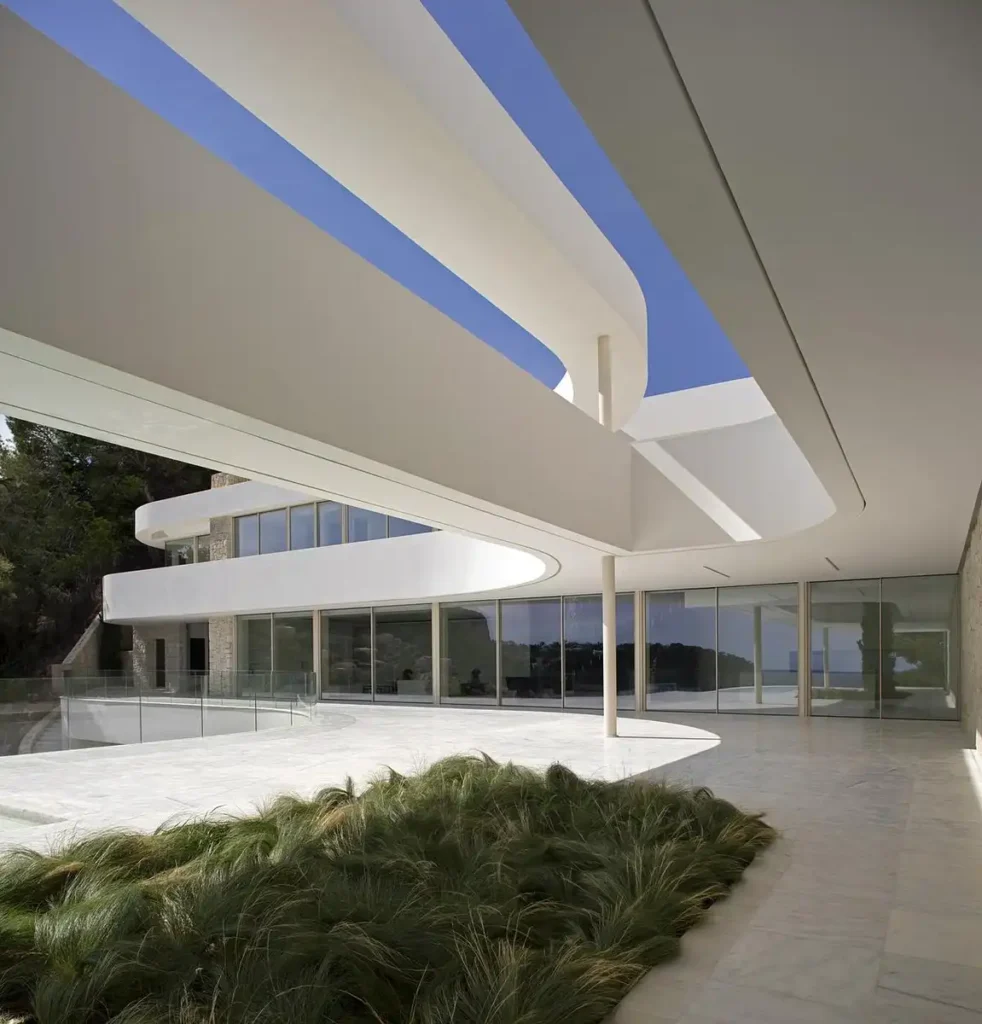 أسطح بيضاء منحنية تُفتح للسماء الزرقاء وتلامس نباتات الحديقة برفق