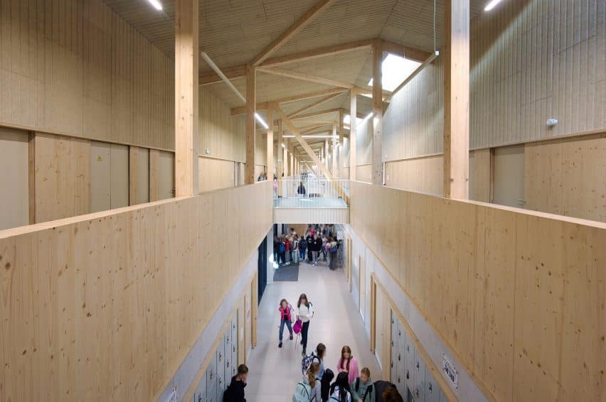 Long interior corridor of the timber-framed school in Cambrai, showcasing its exposed wooden structure and high ceiling with students moving between floors.