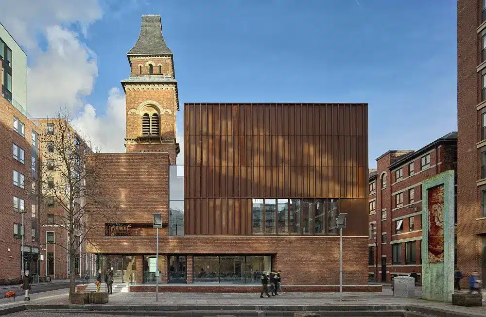 An ecclesiastical building with modern extensions of red brick and Corten panels, showing harmony between historic and contemporary [buildings] in Architectural Regeneration in Manchester.