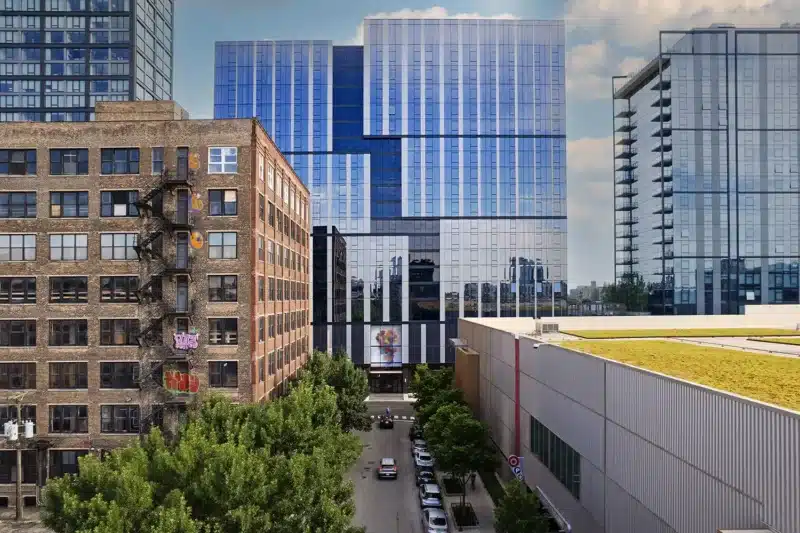 Coppia Tower in Chicago's West Loop, viewed from an elevated perspective, showcasing its modern glass façade alongside historic brick buildings and a green-roofed structure.