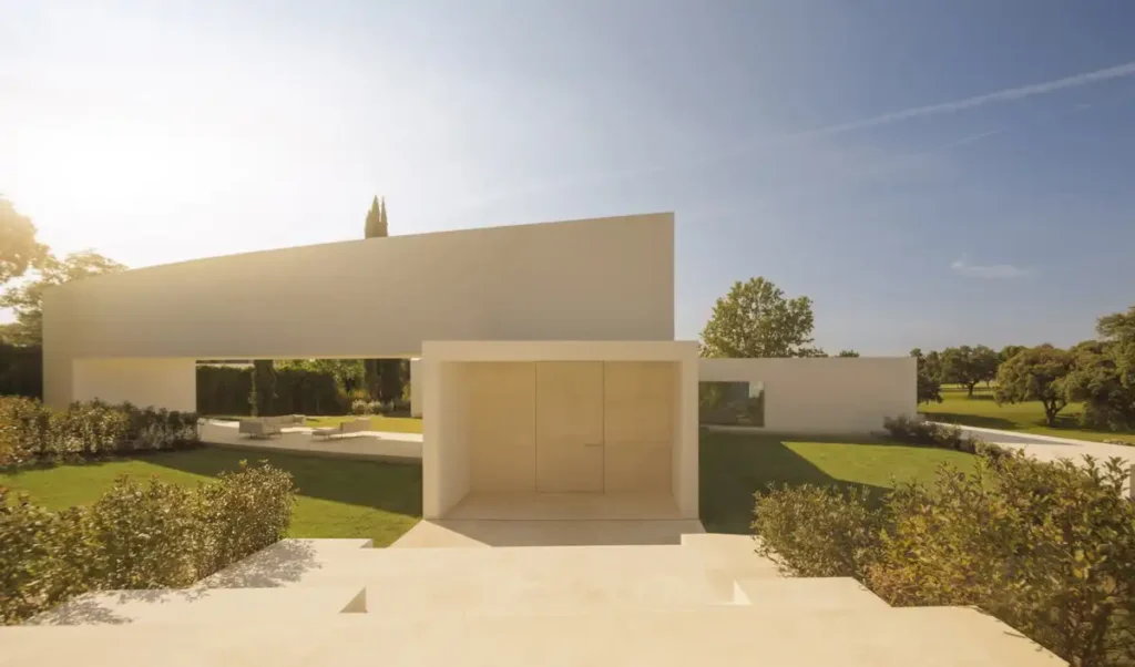 A house that melts into the garden: entrance of a modern villa in Madrid blending curved concrete walls and green spaces through open voids and paved walkways.