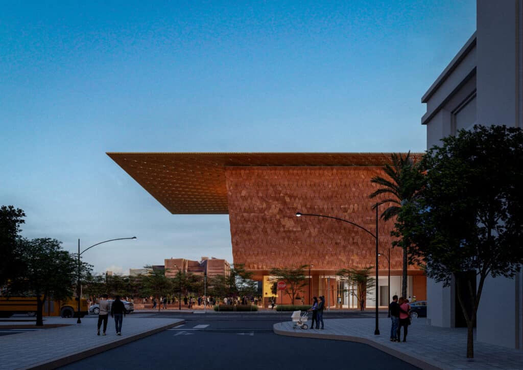 Evening view of the Las Vegas Museum of Art&rsquo;s main entrance, showcasing its textured copper facade and cantilevered wooden canopy over a pedestrian plaza.