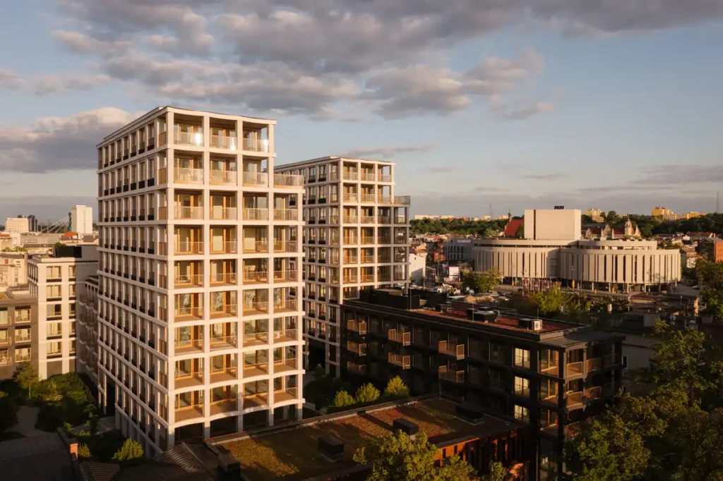 Sunset view of white grid-like apartment towers with wooden loggias in Bydgoszcz&rsquo;s urban landscape.