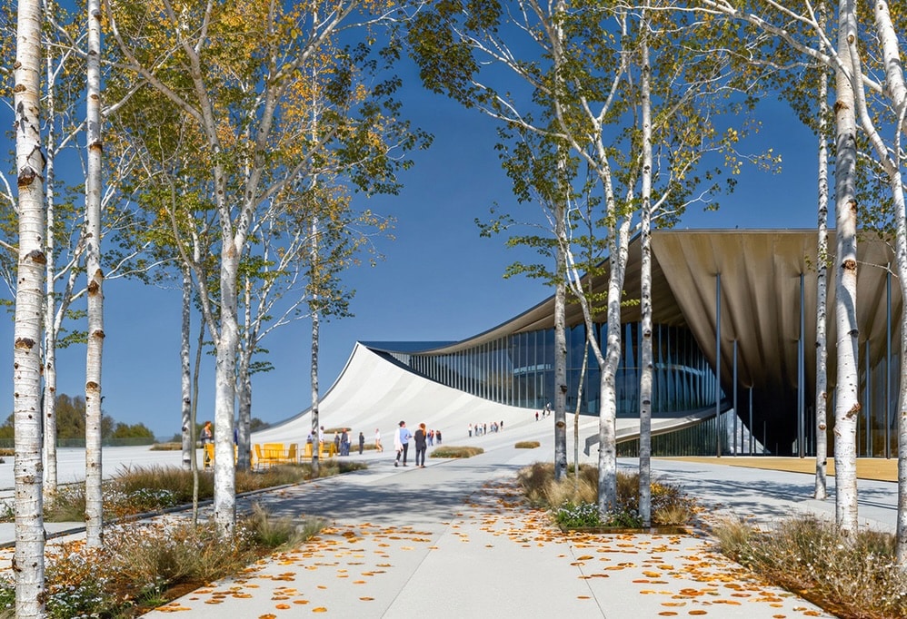 Ulsan Performing Arts Venue exterior view framed by birch trees under a clear blue sky. The architectural design integrates landscape and structure through a sweeping curved roof.