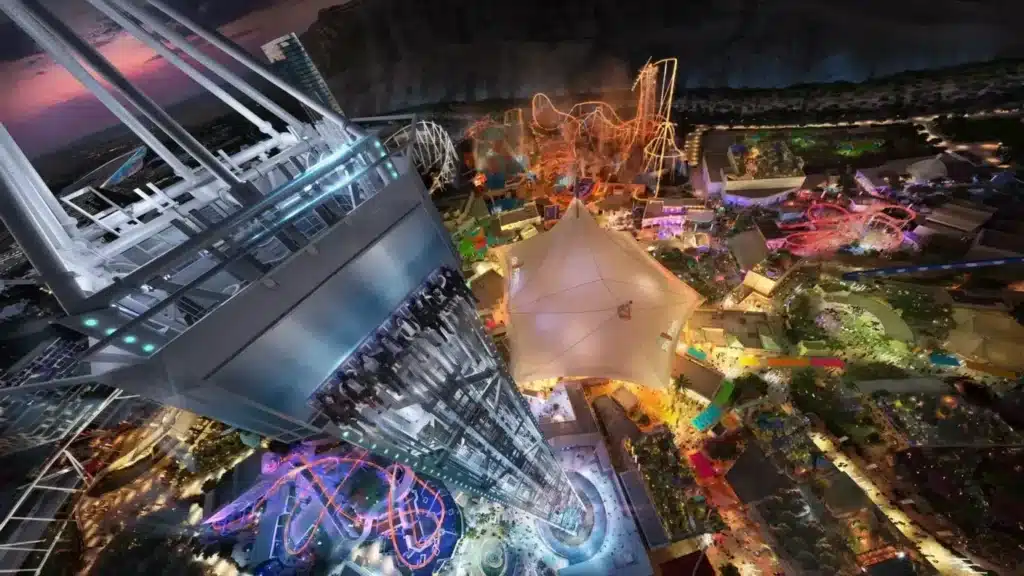 رسم تخطيطي ليلي من الأعلى لمدينة ملاهي Six Flags Qiddiya City في السعودية، يُظهر برج مراقبة مستقبلي، ومسارات سيارات مثيرة مضيئة، ومناطق موضوعية أمام خلفية جبلية صحراوية &mdash; غالبًا ما يُشار إليه في مناقشات دخول يونيفرسال ستوديوز.