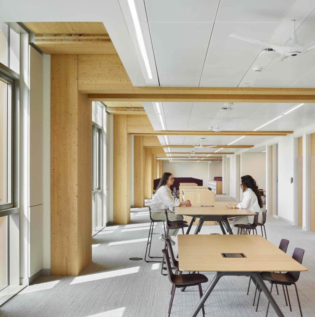 أعمدة خشبية عريضة تدعم سقفًا أبيض، وتُضيء الطاولات بضوء نهاري هادئ